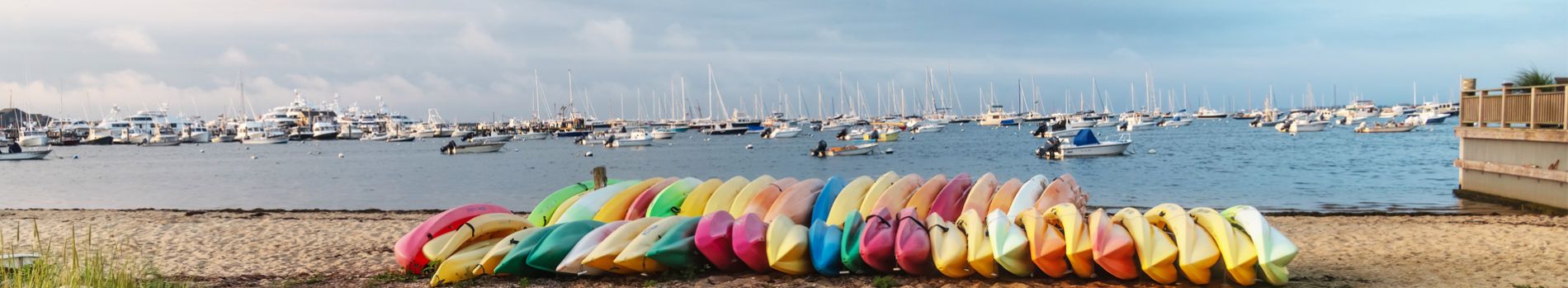 Kayaks stacked on edge across the beach with boats anchored in the marina in the background